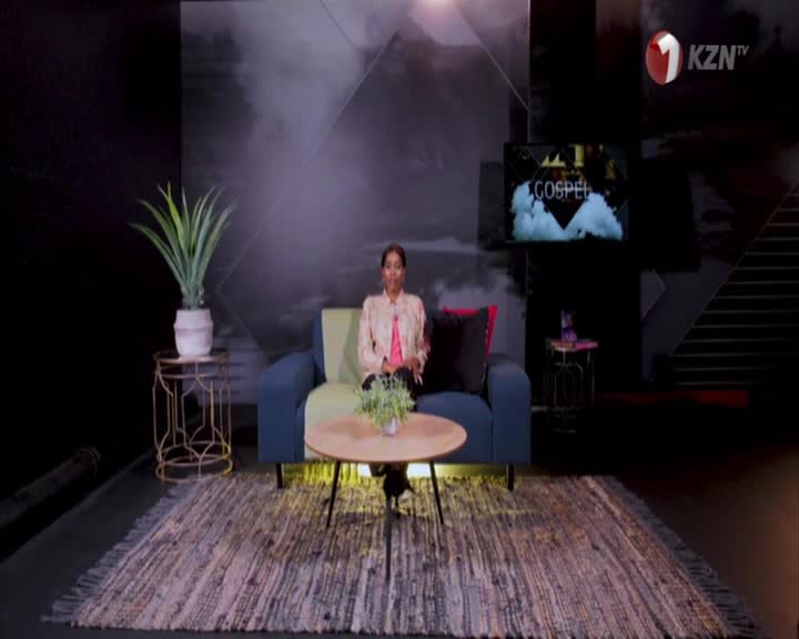 A woman sits on a couch, facing the camera on a 1KZN TV set. Behind her, a screen displays "Gospel" over a cloudy background.
