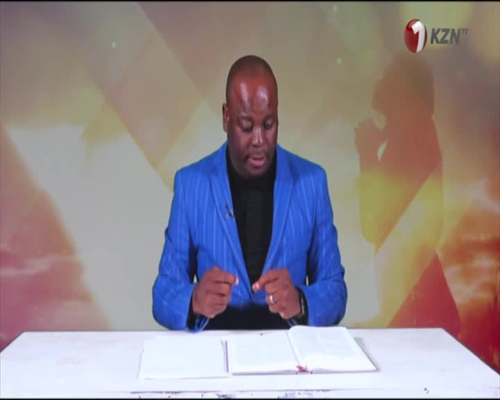 A man in a bright blue suit gestures with his hands over an open book, likely a Bible, on a desk. The 1KZN TV logo is visible in the corner, and a soft, golden light shines behind him on the set.
