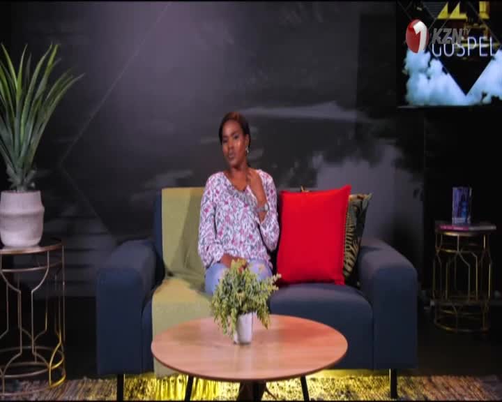 A woman in a floral top sits on a couch, looking directly at the camera. Behind her, the 1KZN Gospel logo is visible on a screen, indicating this is a South African television studio.
