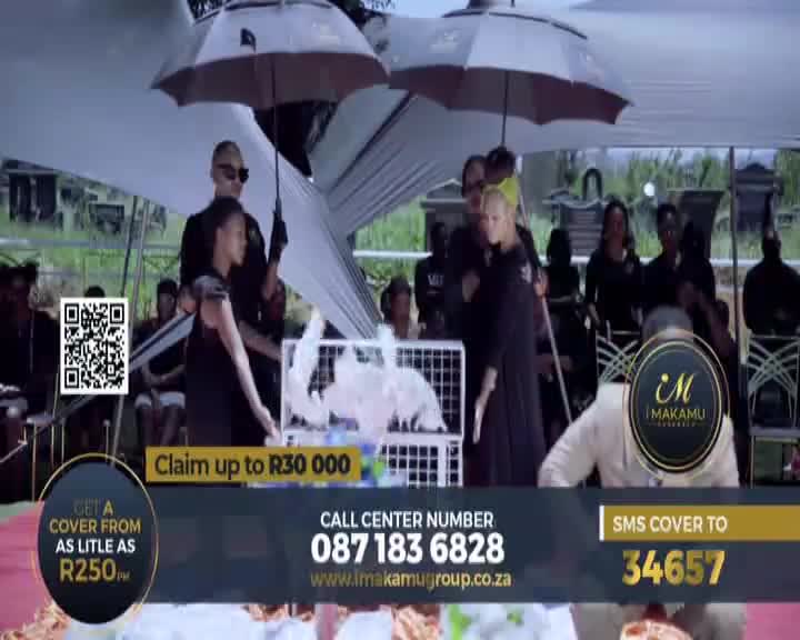 Underneath a large white umbrella, a woman in black gestures toward a cage filled with white objects. The scene is set outdoors, with a crowd of people watching, and a 1KZN TV advertisement for insurance is visible.
