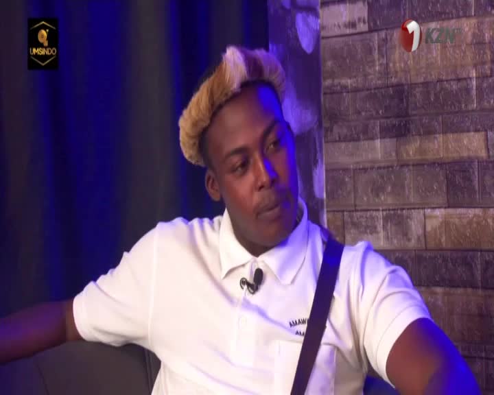 The man in the white polo shirt is speaking, his gaze directed off-camera. The 1KZN TV logo is visible, and the set has a dark blue backdrop.
