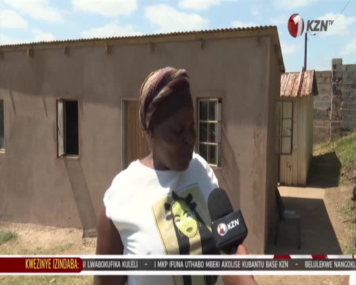 A woman is speaking into a KZN TV microphone outside a small house. The news ticker at the bottom of the screen scrolls with Zulu text. A woman is speaking into a KZN TV microphone outside a small house. The news ticker at the bottom of the screen scrolls with Zulu text.