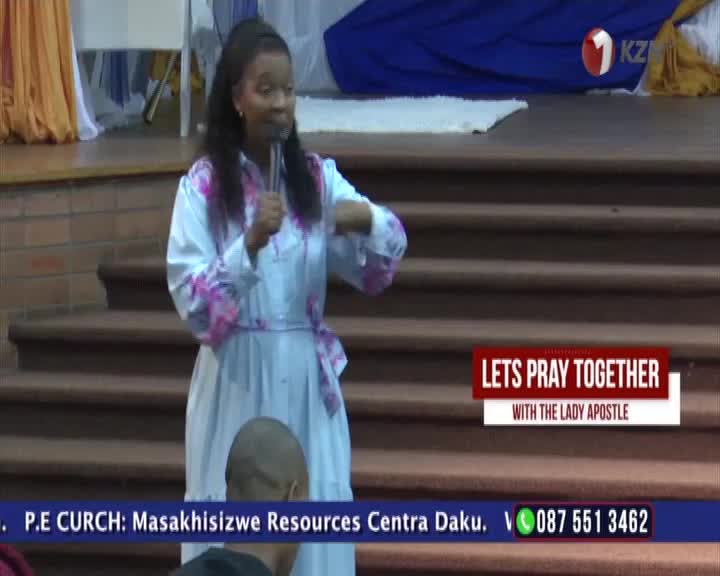 A woman in a light blue robe with pink floral accents speaks into a microphone, gesturing with her hands. The 1KZN TV logo appears in the upper right corner, and a banner below reads "LETS PRAY TOGETHER WITH THE LADY APOSTLE." A woman in a light blue robe with pink floral accents speaks into a microphone, gesturing with her hands. The 1KZN TV logo appears in the upper right corner, and a banner below reads "LETS PRAY TOGETHER WITH THE LADY APOSTLE."
