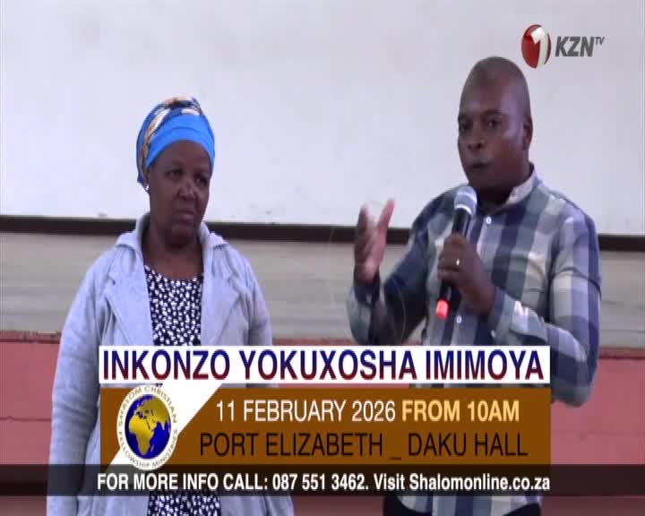 A man speaks into a microphone, his hands gesturing as he addresses an unseen audience. Beside him, a woman stands attentively, her gaze directed forward. A man speaks into a microphone, his hands gesturing as he addresses an unseen audience. Beside him, a woman stands attentively, her gaze directed forward.