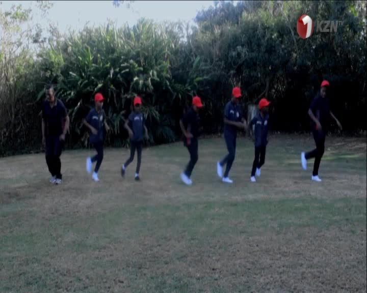 A group of people in red caps and dark shirts are jogging in unison across a grassy field. They're moving together, a rhythmic procession against the backdrop of lush green foliage. A group of people in red caps and dark shirts are jogging in unison across a grassy field. They're moving together, a rhythmic procession against the backdrop of lush green foliage.