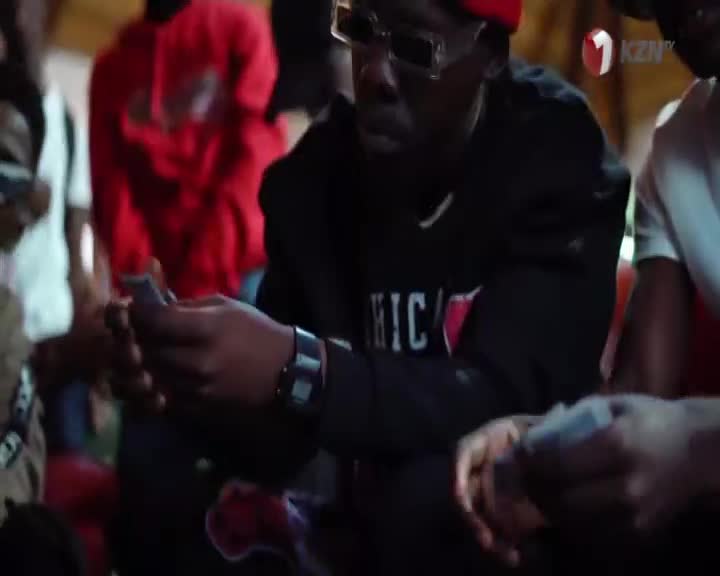 A group of men are gathered, intently focused on the cards in their hands. The 1KZN TV logo is visible in the background, suggesting this scene is part of a broadcast from South Africa. A group of men are gathered, intently focused on the cards in their hands. The 1KZN TV logo is visible in the background, suggesting this scene is part of a broadcast from South Africa.