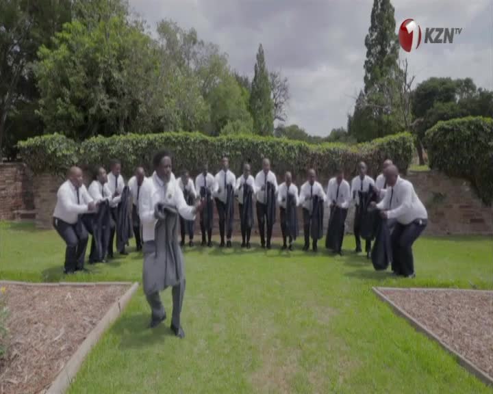 A group of men in white shirts and dark trousers are performing a synchronized dance, holding dark jackets. The KZN TV logo appears in the top right corner. A group of men in white shirts and dark trousers are performing a synchronized dance, holding dark jackets. The KZN TV logo appears in the top right corner.
