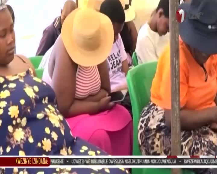 A group of people sit attentively, some with heads bowed, under a tent. A 1KZN TV logo is visible in the upper right corner. A group of people sit attentively, some with heads bowed, under a tent. A 1KZN TV logo is visible in the upper right corner.