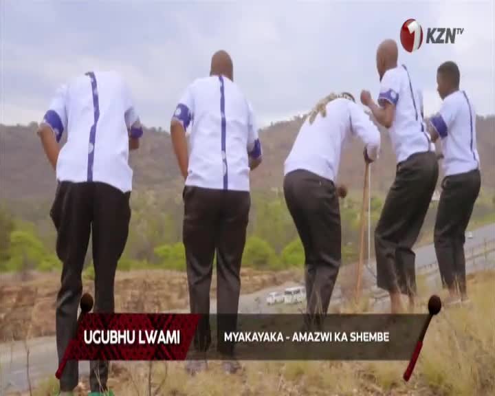 Five men in white shirts with blue trim stand on a hillside, their backs to the camera. One man leans on a long stick as the others shift their weight. The KZN TV logo appears in the upper right corner. Five men in white shirts with blue trim stand on a hillside, their backs to the camera. One man leans on a long stick as the others shift their weight. The KZN TV logo appears in the upper right corner.