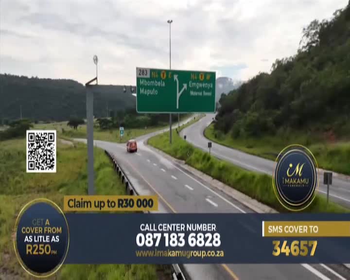 A lone red car travels along a highway in South Africa, heading towards a green signpost indicating routes to Mbombela and Maputo. The road curves through a landscape of rolling green hills under a cloudy sky. A lone red car travels along a highway in South Africa, heading towards a green signpost indicating routes to Mbombela and Maputo. The road curves through a landscape of rolling green hills under a cloudy sky.