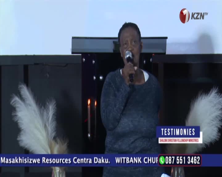 A woman stands at a podium, speaking into a microphone. Two tall, feathery plumes flank her, and a KZN TV logo appears in the upper right corner.