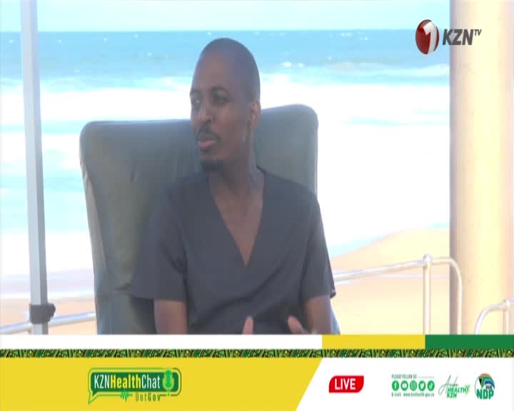 A man in a dark shirt sits in a canvas chair, facing away from the ocean. The KZN TV logo appears in the upper right corner.