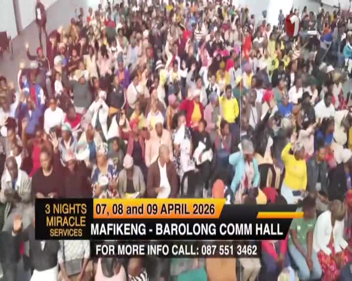 A large crowd fills the hall, many with hands raised towards the stage. The 1KZN TV broadcast announces miracle services in Mafikeng.