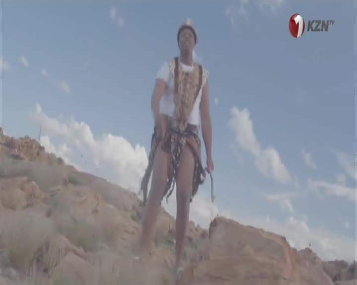 A man in traditional Zulu attire walks across a rocky, dry landscape under a vast blue sky. The 1KZN TV logo appears in the upper right corner. A man in traditional Zulu attire walks across a rocky, dry landscape under a vast blue sky. The 1KZN TV logo appears in the upper right corner.
