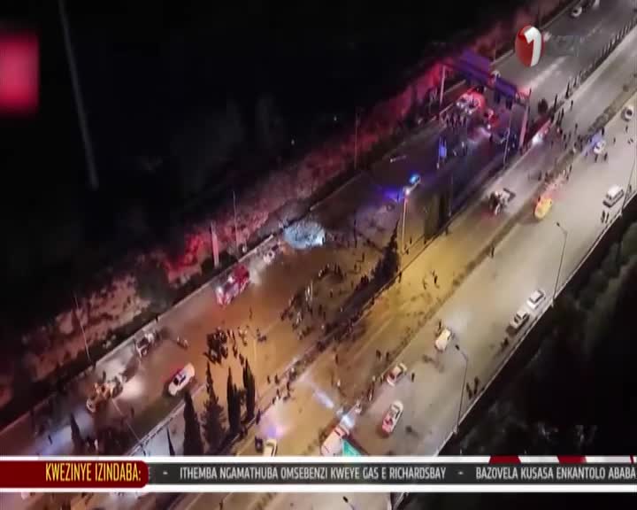 Emergency vehicles are gathered on a bridge, their lights flashing. People are standing around, some near what appears to be a damaged vehicle. Emergency vehicles are gathered on a bridge, their lights flashing. People are standing around, some near what appears to be a damaged vehicle.