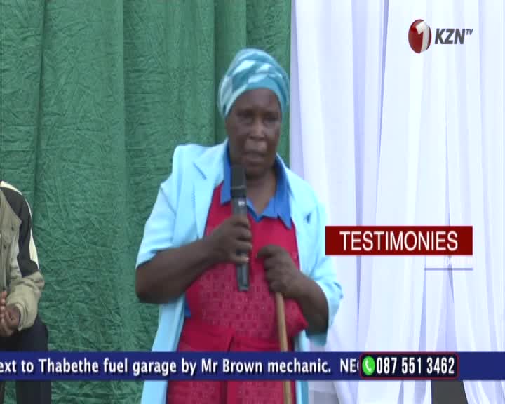 A woman in a blue headscarf and light blue jacket speaks into a microphone, holding a wooden stick. The KZN TV logo is visible in the upper right corner.