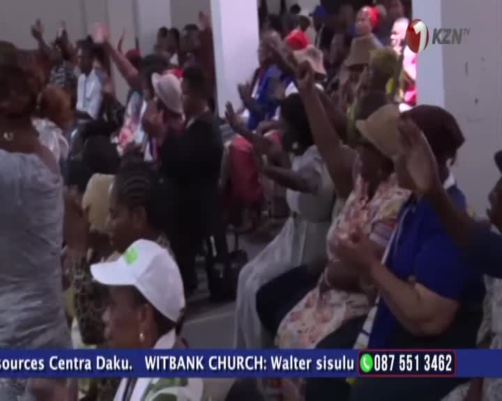 Hands are raised in a church service in Witbank, South Africa. A woman in a white cap looks towards the front, her hands clasped. Hands are raised in a church service in Witbank, South Africa. A woman in a white cap looks towards the front, her hands clasped.