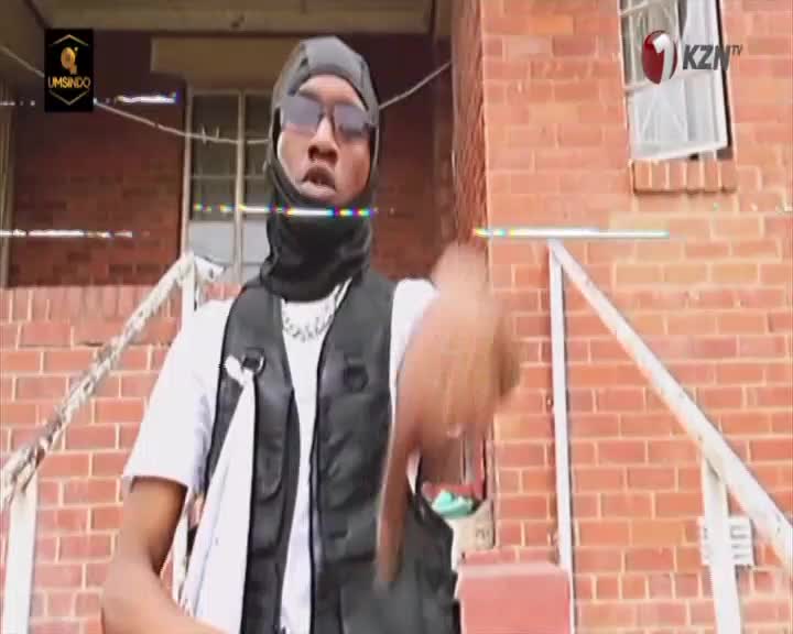 A young man in a black durag and vest gestures with his thumb down. The KZN TV logo appears in the corner of the brick building behind him. A young man in a black durag and vest gestures with his thumb down. The KZN TV logo appears in the corner of the brick building behind him.