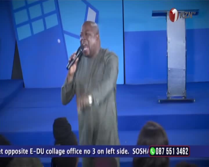 A man in a green tunic holds a microphone, his mouth open as he speaks into it. The 1KZN TV logo is visible on a podium behind him. A man in a green tunic holds a microphone, his mouth open as he speaks into it. The 1KZN TV logo is visible on a podium behind him.