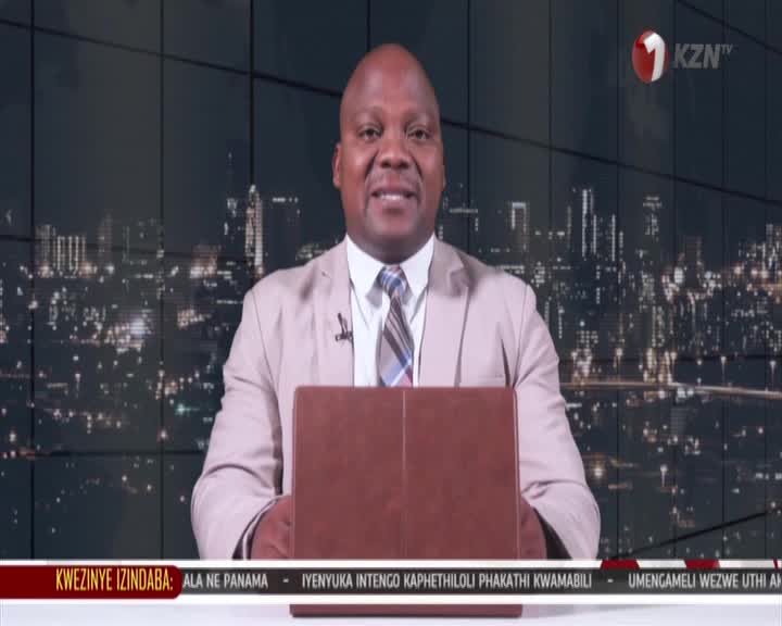 A man in a light suit and tie stands behind a brown lectern, a city skyline at night behind him. The KZN TV logo is visible in the upper right corner.