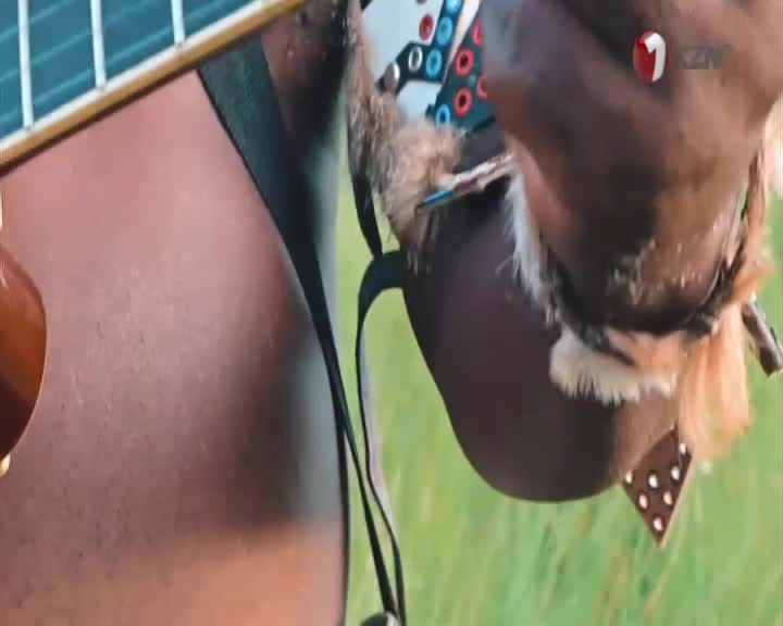 A man, adorned in traditional Zulu attire with beaded accents, plays a guitar. The 1KZN TV logo is visible in the corner.