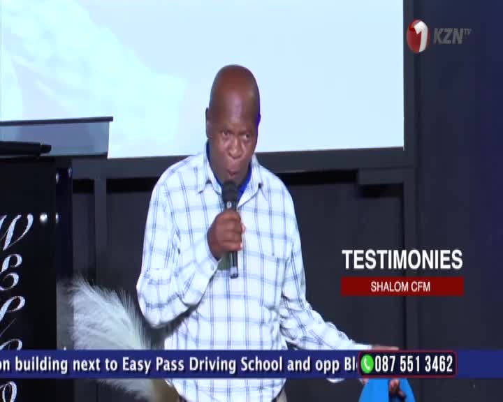 A man in a checkered shirt speaks into a microphone on a stage, with the 1KZN TV logo visible. The words "TESTIMONIES" and "SHALOM CFM" appear on a screen behind him.