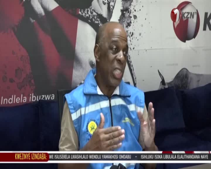 A man in a blue vest speaks animatedly, his hands gesturing. The KZN TV logo is visible behind him.