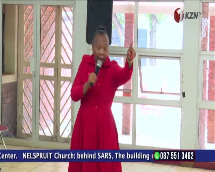 A woman in a bright red dress holds a microphone and gestures with her left hand. She speaks with conviction, her voice amplified, as the KZN TV logo appears in the corner.