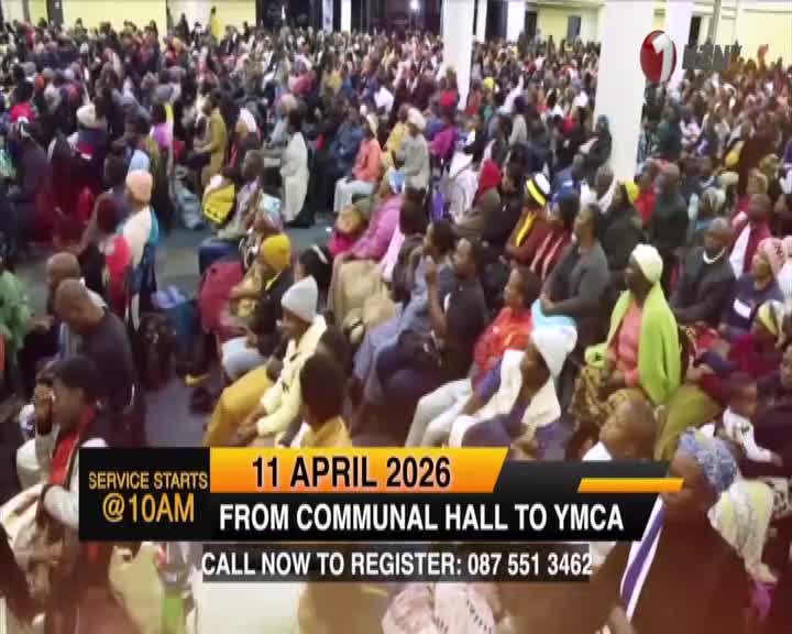 A large congregation fills the hall, many wearing bright colours. The 1KZN TV broadcast overlays information about a service starting at 10 AM on April 11, 2026, moving from the Communal Hall to the YMCA.