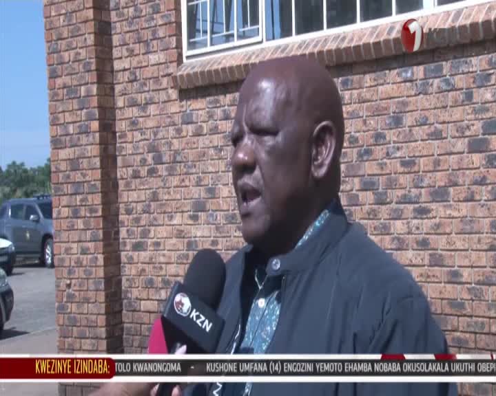 A man speaks into a KZN microphone outside a brick building. The lower third of the screen displays Zulu text. A man speaks into a KZN microphone outside a brick building. The lower third of the screen displays Zulu text.