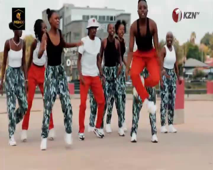 A group of dancers in vibrant red pants and patterned trousers are moving in unison. One dancer leaps high into the air, arms outstretched, as the KZN TV logo appears.
