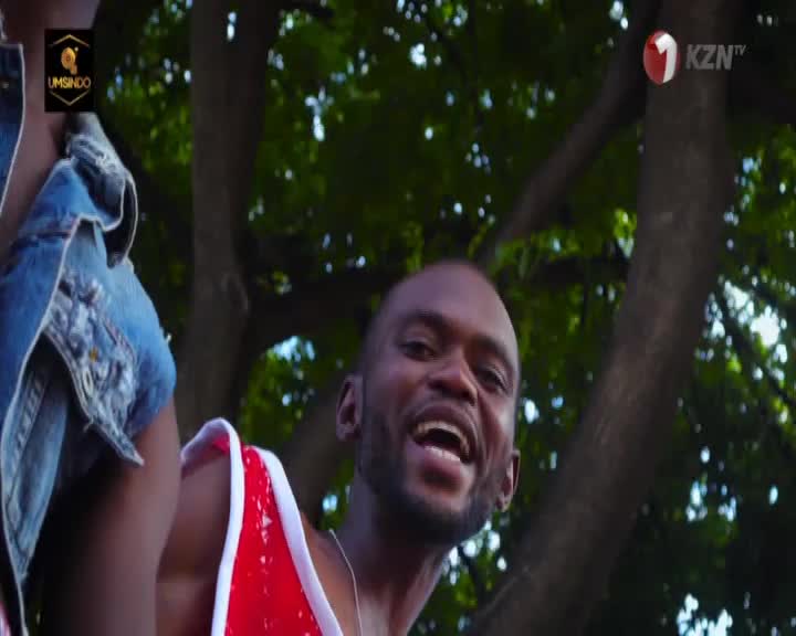 A man with a wide smile, wearing a red and white sequined top, is looking directly at me. Beside him, a person in a denim jacket is partially visible, with the KZN TV logo in the corner.