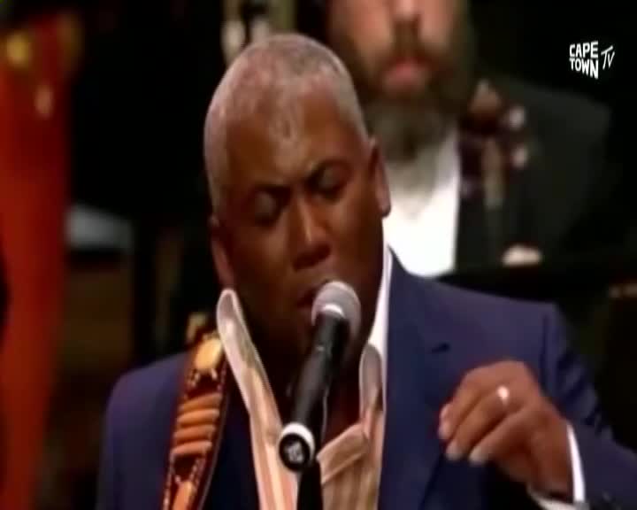 The singer, dressed in a blue suit, is leaning into the microphone, his face lit by the stage lights. Cape Town TV's logo is visible as he performs, his voice filling the space.
