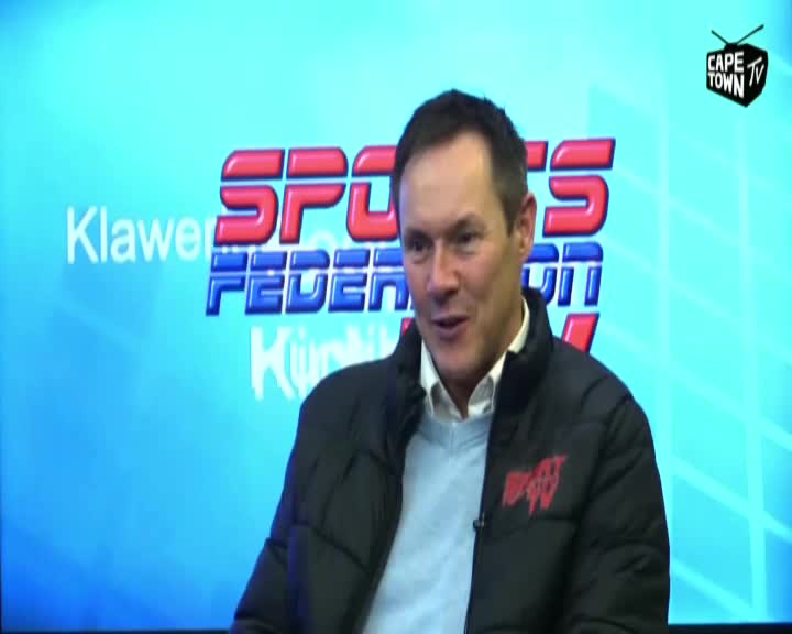 The man in the black jacket is speaking, his mouth open in mid-sentence. Behind him, a blue backdrop displays the "Sports Federation" logo, and the Cape Town TV logo is visible in the corner.
