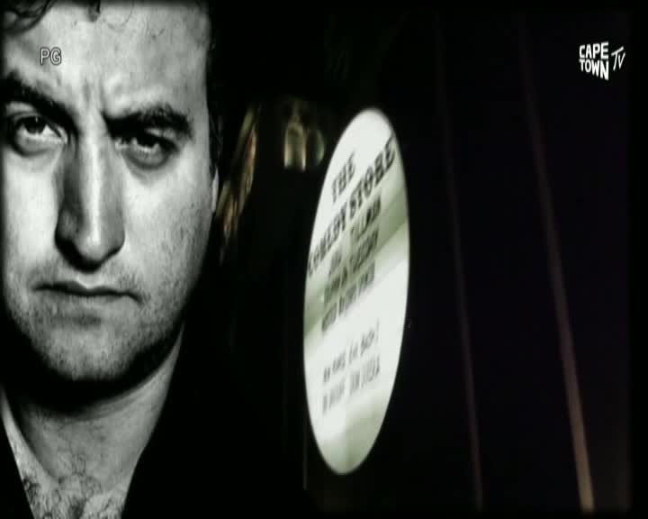 A man stares intently at the camera, his face filling the screen alongside a sign for The Comedy Store. The Cape Town TV logo sits in the corner, marking the broadcast's origin.
