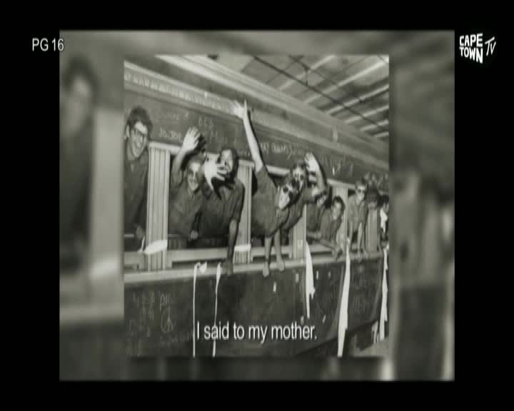 From the Cape Town TV screen, a black and white image shows a train car filled with people leaning out the windows. Some are waving, while one man has his arm raised high, as if shouting.
