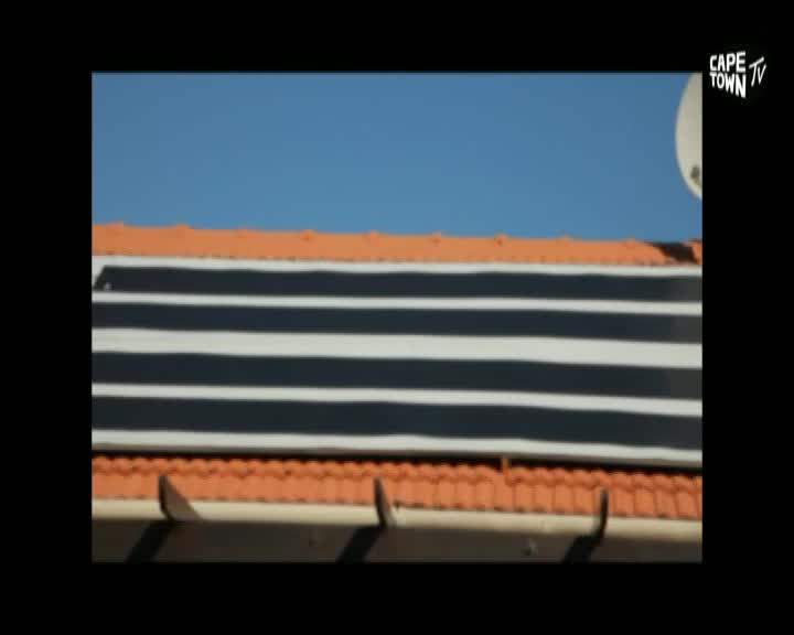 The roof of a building, with its orange tiles and black-and-white panels, sits against a clear blue sky. A Cape Town TV logo is visible in the corner.
