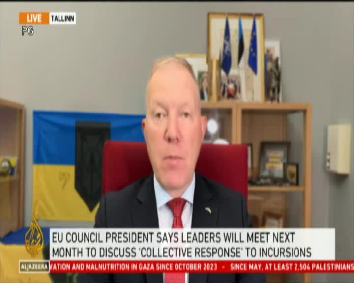 A man in a suit and tie is speaking directly to the camera, with a flag behind him. The Al Jazeera logo is visible, and a headline scrolls across the bottom of the screen.
