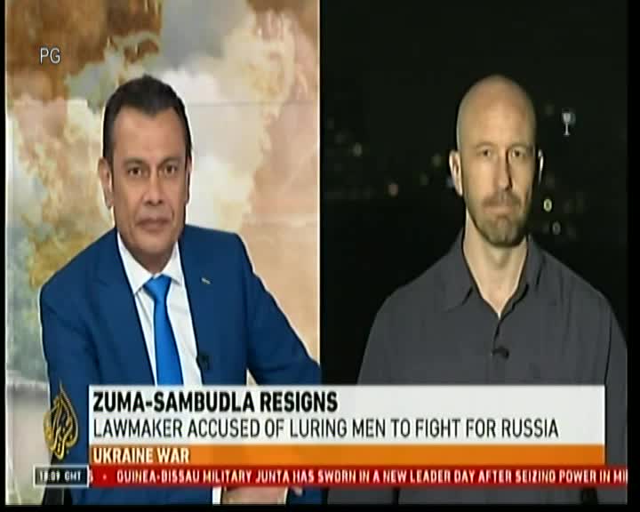 A news anchor in a blue suit is speaking, while a man in a gray shirt looks on from a separate screen. The chyron at the bottom of the screen details the resignation of Zuma-Sambudla and the Ukraine war.
