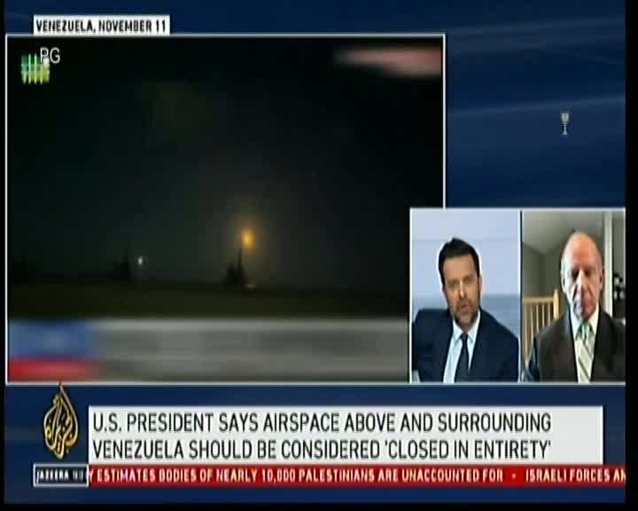 Two men in suits are discussing the U.S. President's stance on Venezuelan airspace, while a grainy, nighttime shot of a runway plays in the background. The Al Jazeera logo and a news ticker below provide context to the broadcast.
