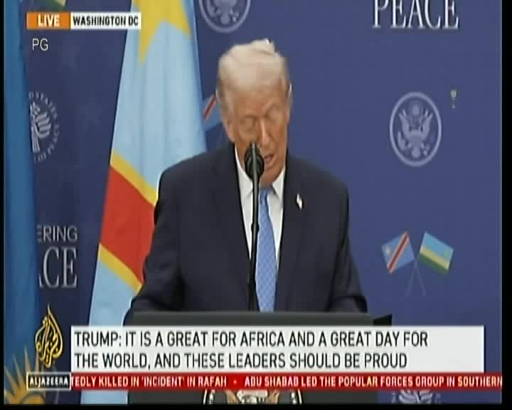 A man in a blue suit speaks into a microphone, his head tilted slightly down. The Al Jazeera banner at the bottom of the screen reports on the news, with the live feed originating from Washington D.C.
