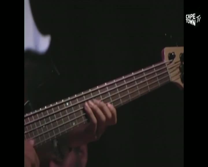A hand presses down on the fretboard of a bass guitar, fingers sliding between the metal frets. The Cape Town TV logo appears in the corner, a reminder of where this performance is being broadcast. A hand presses down on the fretboard of a bass guitar, fingers sliding between the metal frets. The Cape Town TV logo appears in the corner, a reminder of where this performance is being broadcast.