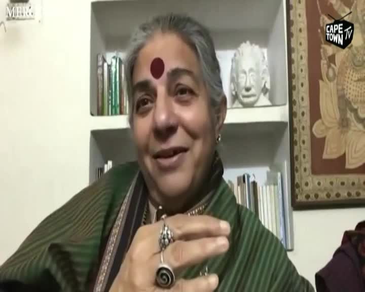 A woman with a red bindi on her forehead speaks animatedly, her hands gesturing. Behind her, shelves hold books and a bust of Albert Einstein, with a Cape Town TV logo visible. A woman with a red bindi on her forehead speaks animatedly, her hands gesturing. Behind her, shelves hold books and a bust of Albert Einstein, with a Cape Town TV logo visible.
