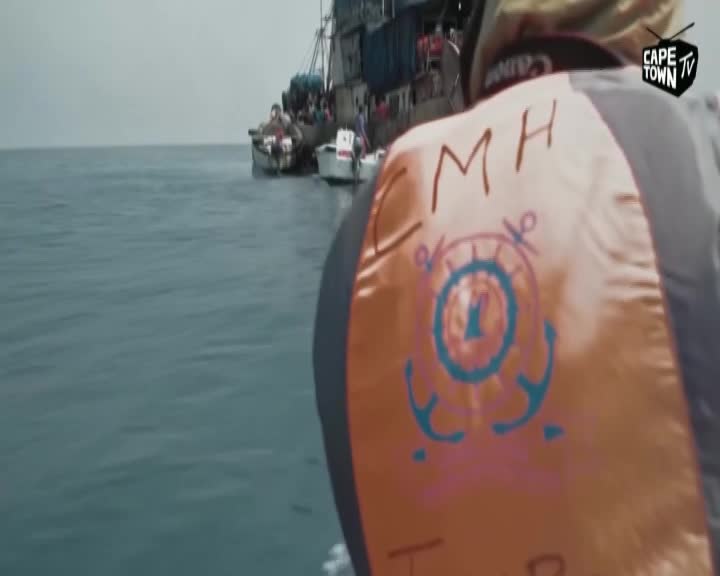 Several small boats cluster around a larger vessel, their passengers visible on deck. The Cape Town TV logo is visible on the back of a life vest in the foreground.