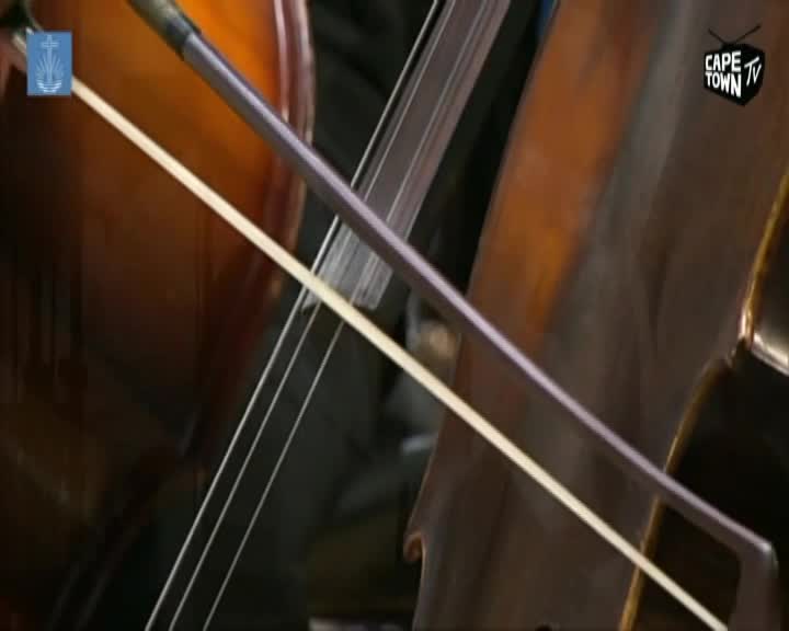 A cello bow glides across the strings, its white horsehair a stark contrast against the instrument's warm wood. The Cape Town TV logo is visible in the corner, a reminder of the broadcast.