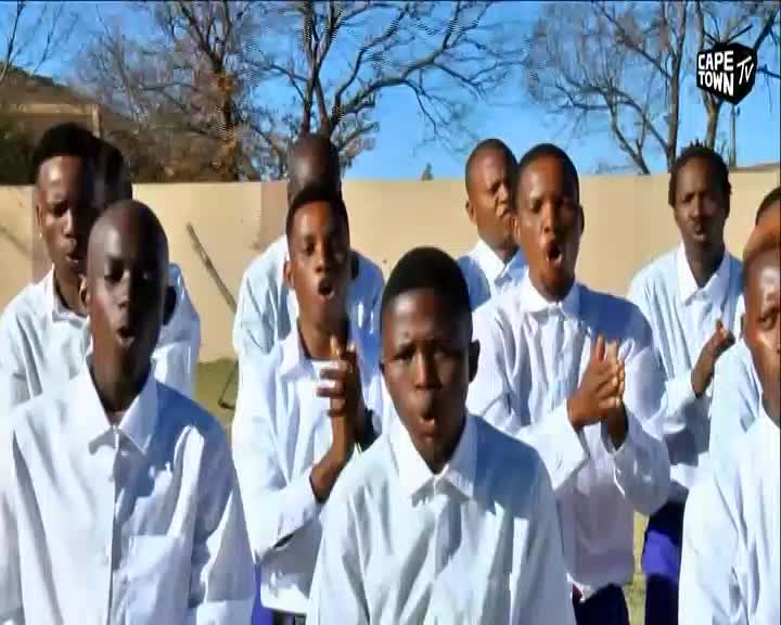 A group of young men in white shirts stand together, their mouths open in song. The Cape Town TV logo appears in the corner of the frame.