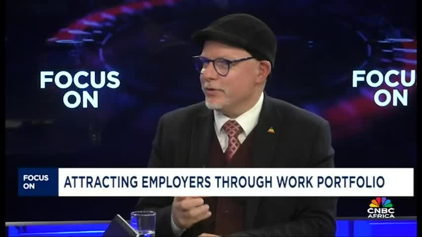A man in a suit and a black cap gestures with his right hand while speaking on CNBC Africa. The screen behind him reads "Focus On" and the topic "Attracting Employers Through Work Portfolio."
