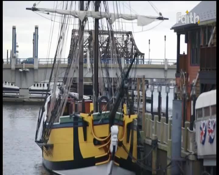 A tall ship with yellow trim is docked, its rigging a web against the overcast sky. Beyond the masts, a bridge rises, and a small "Faith" logo is visible in the corner.
