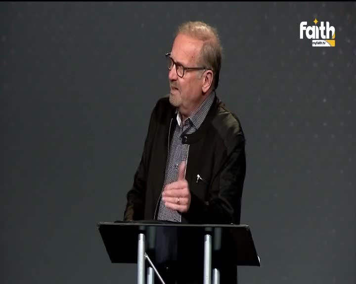 A man in a black jacket gestures with his right hand, speaking from behind a podium. The Faith TV logo is visible in the corner, and the background is a plain, dark gray.
