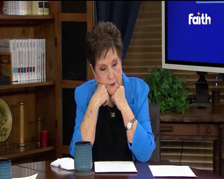 A woman in a blue blazer rests her chin on her hands, looking down at a document on the table. The "Faith" logo is visible on a screen behind her.
